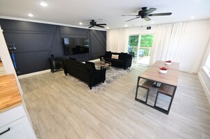 Uma sala de estar moderna com televisão de tela plana, sofás pretos, uma mesa de centro e uma mesa de jantar com cadeiras.