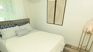A bedroom with a bed, a chandelier, a window with curtains, and a wall-mounted artwork. - Wynter Luxe  (Peachtree City)