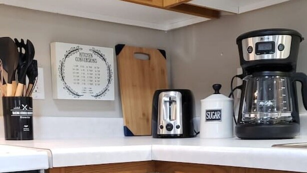 A kitchen with wooden cabinets, a white countertop, a coffee maker, a toaster, and a cutting board.