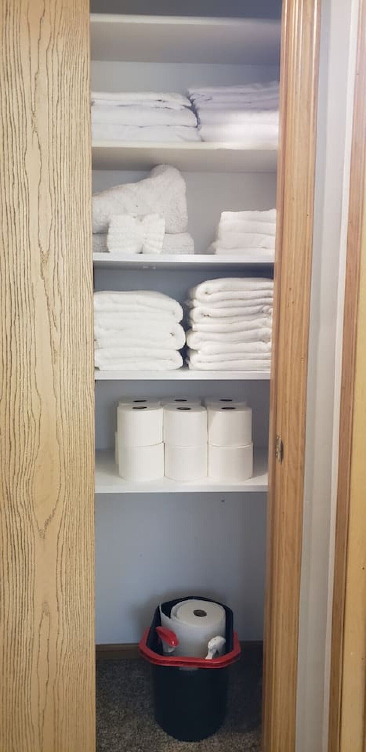 A closet with shelves containing folded towels and toilet paper.