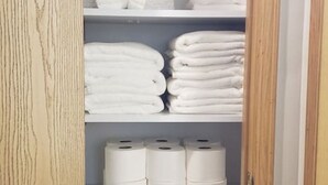 A closet with shelves containing folded towels and toilet paper.