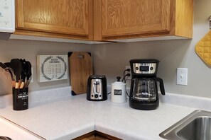 A kitchen with wooden cabinets, a toaster, a coffee maker, and a sugar container.