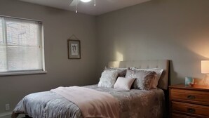 A bedroom with a bed, a dresser, a window with blinds, and a framed picture on the wall.