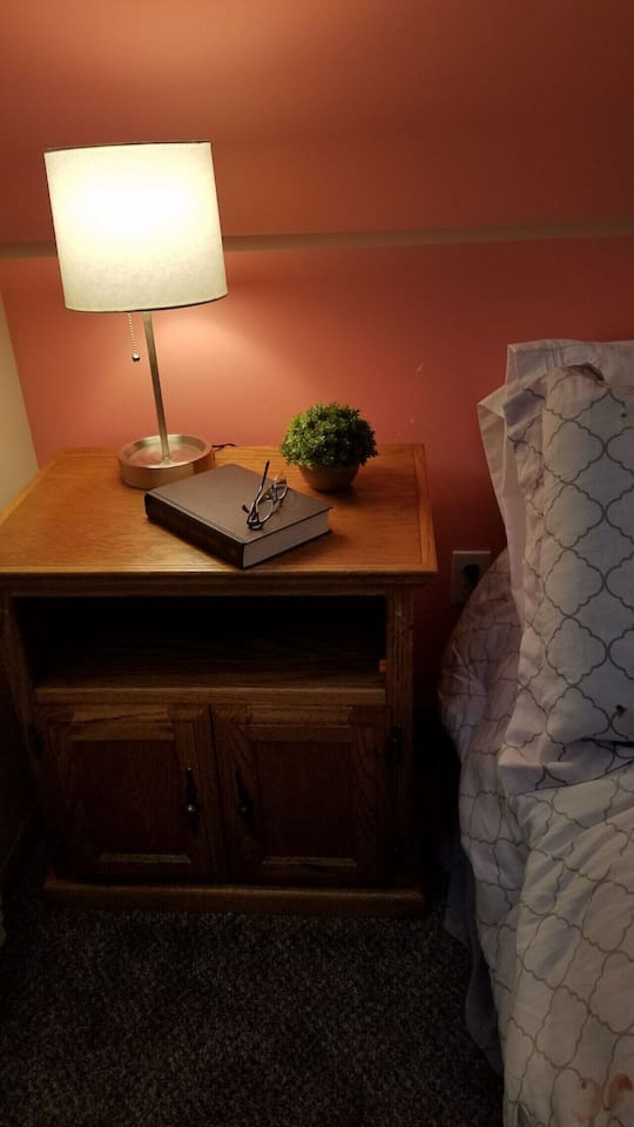 Une table de chevet en bois, avec une lampe, un livre et une petite plante.