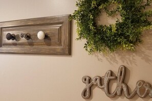 A wall with a wooden plaque, a wreath, and a metal word 'gather' on a beige wall.