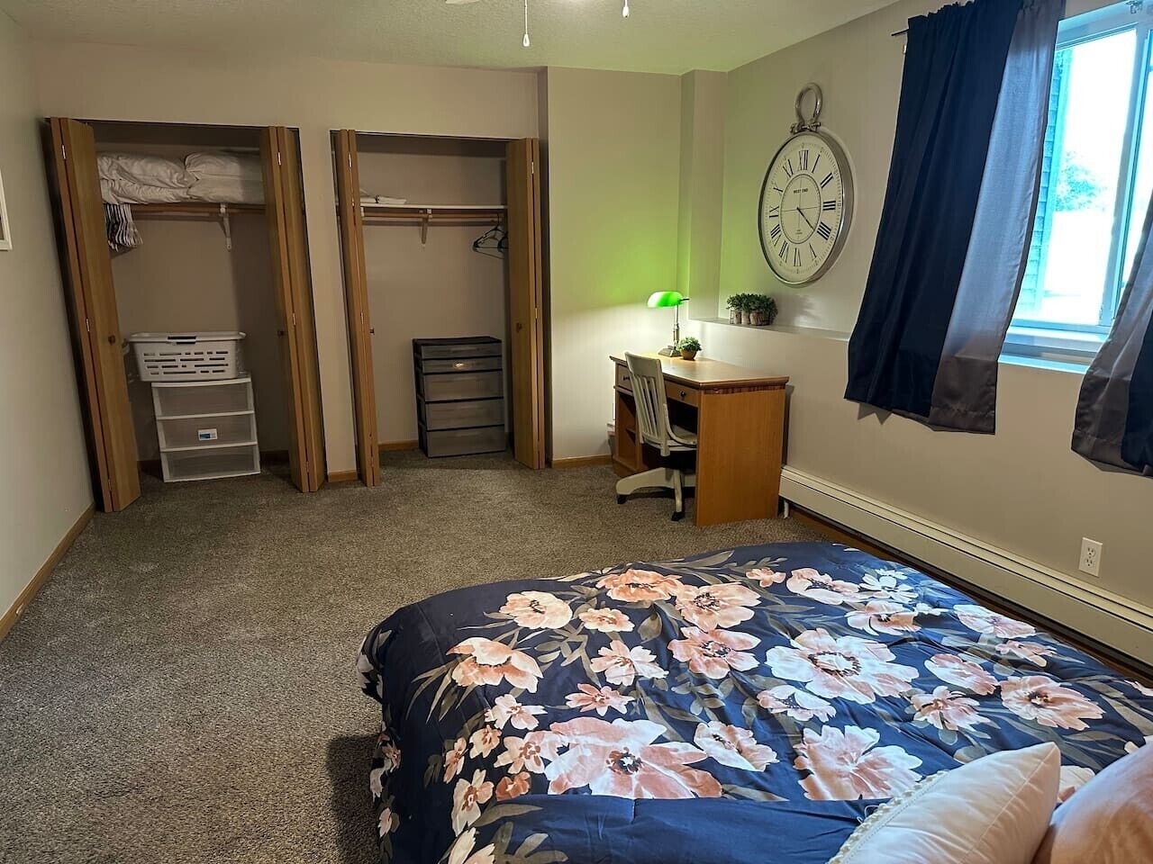 A bedroom with a bed, a desk, a chair, a wardrobe, and a clock on the wall.