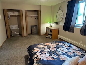 A bedroom with a bed, a desk, a chair, a wardrobe, and a clock on the wall.