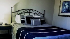 A neatly made bed with a dark blue and white striped bedspread, a metal headboard, and a bedside table with a lamp.