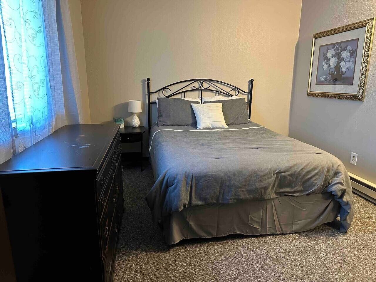 A bedroom with a bed, dresser, nightstand, lamp, and a framed picture on the wall.