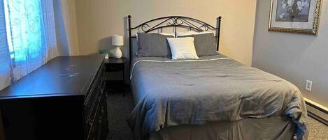 A bedroom with a bed, dresser, nightstand, lamp, and a framed picture on the wall.