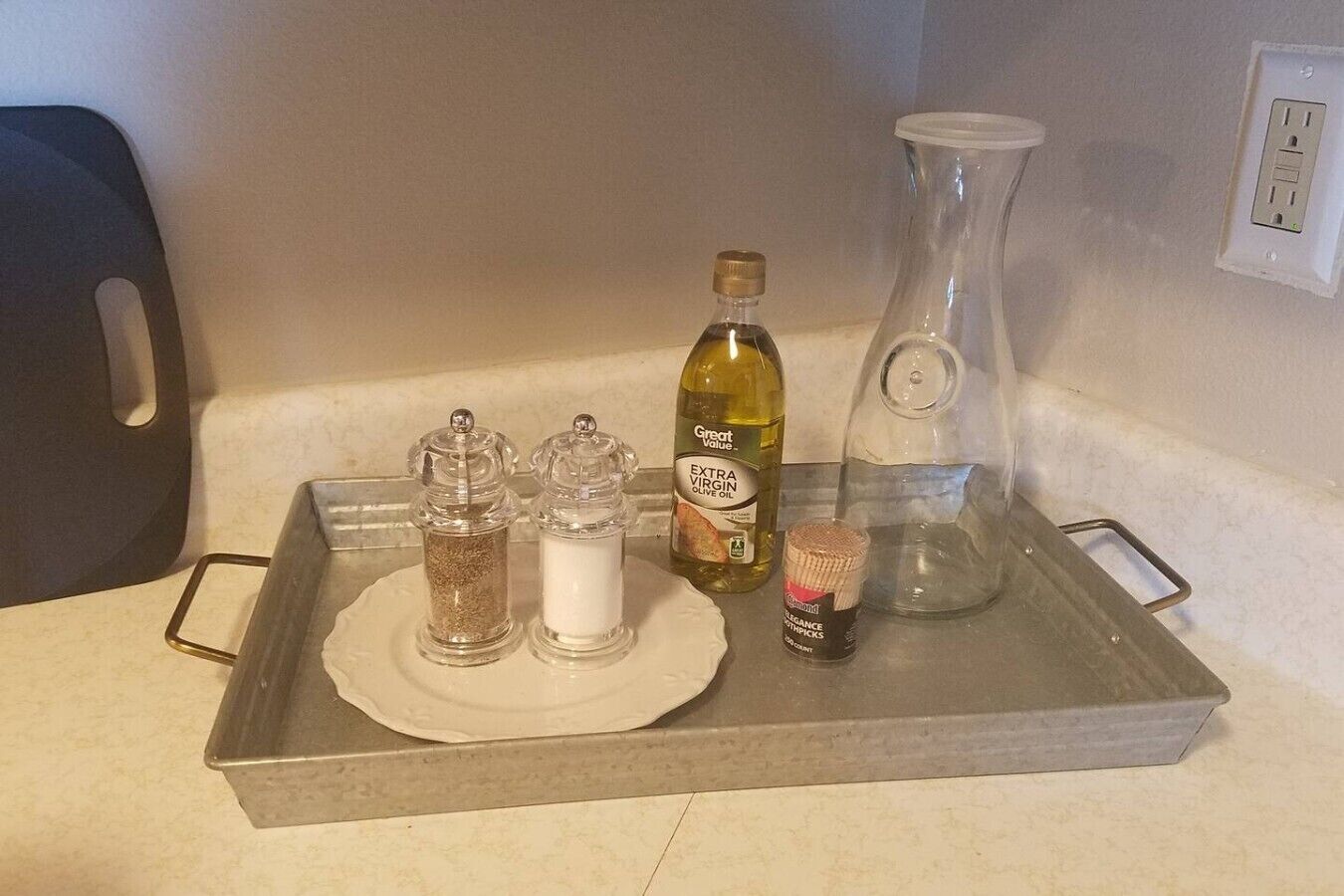 A kitchen counter with a tray holding various items including a bottle of extra virgin olive oil, a glass bottle, salt and pepper shakers, and a small container.