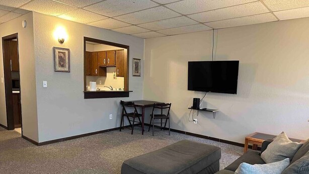 A compact living space with a kitchenette, a flat-screen TV mounted on the wall, a sofa, and a small table with chairs.