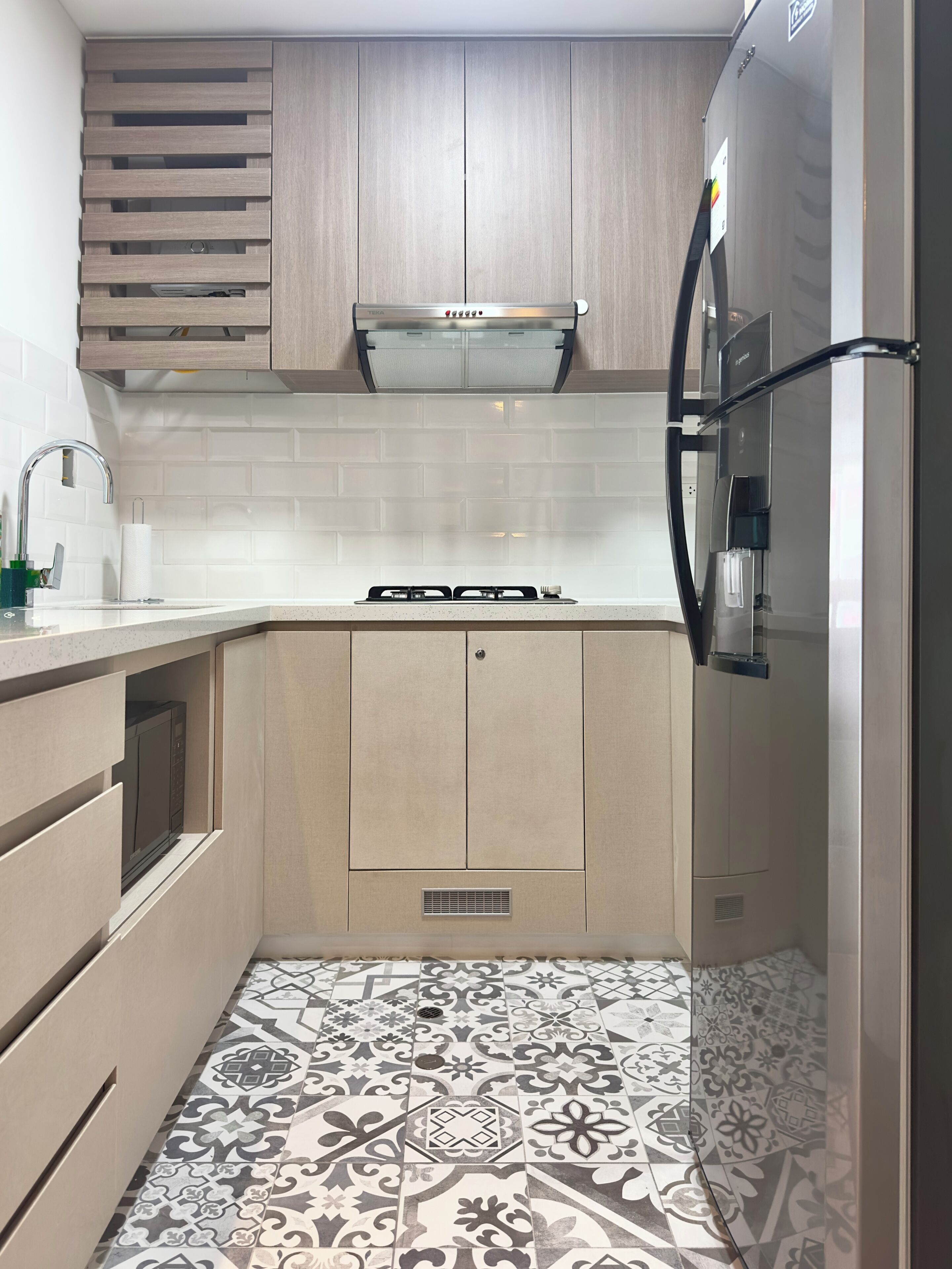 A compact kitchen with a built-in oven, a stainless steel refrigerator, and a patterned tile floor.