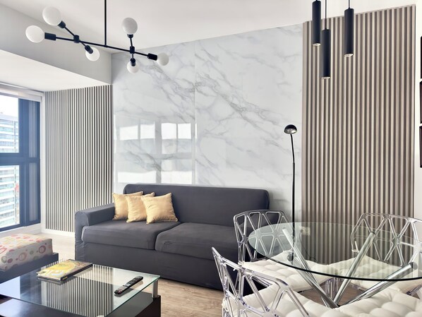 Ein modernes Wohnzimmer mit grauem Sofa, einem transparenten Glastisch und einem außergewöhnlichen Glasstuhl.