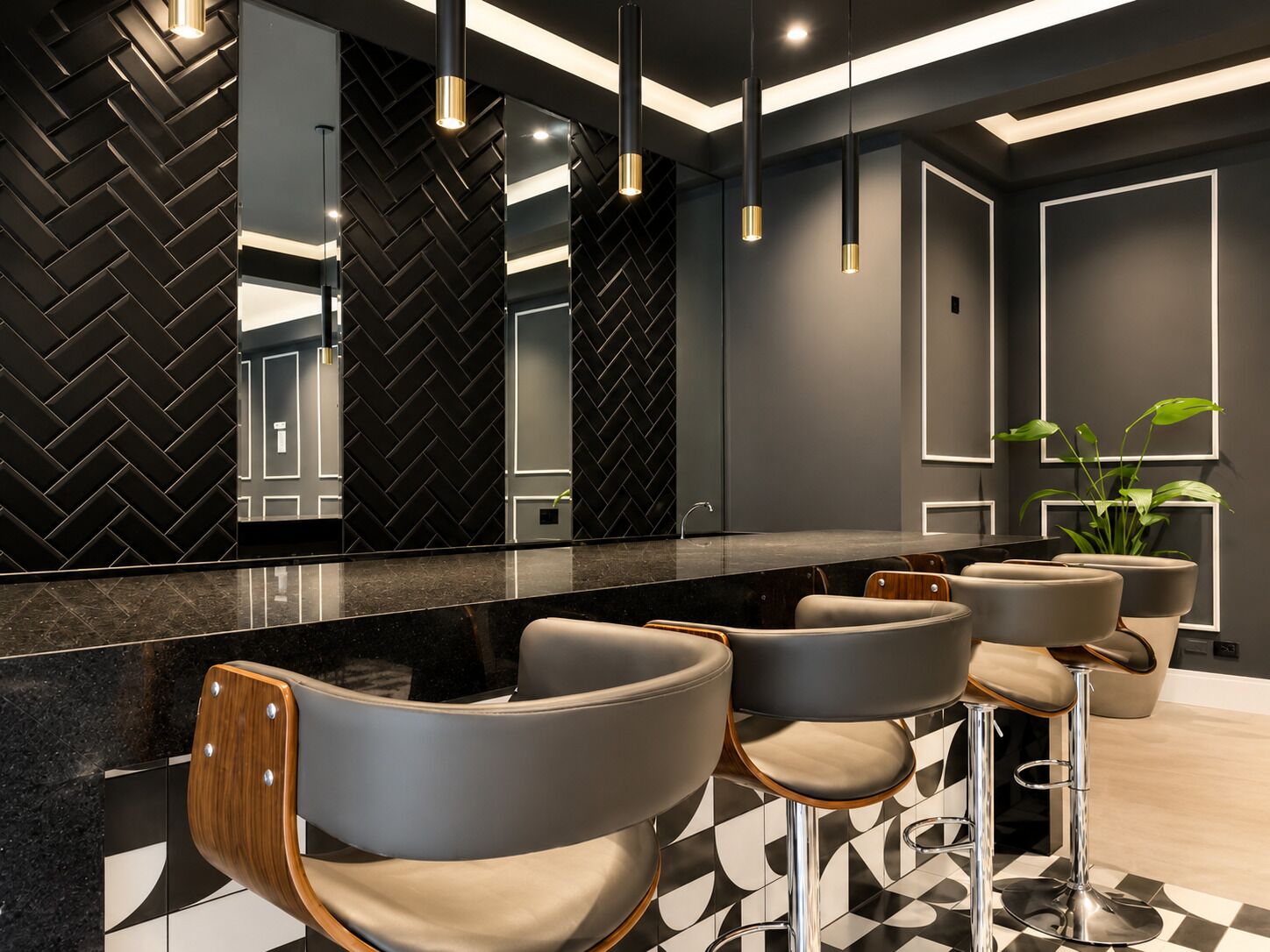 Une salle de bain moderne avec un mur orné d’un motif en chevrons noirs, un grand miroir et un comptoir en marbre. On y trouve trois chaises grises avec des détails en bois et des pieds chromés.