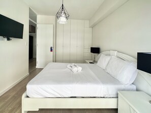 Ein Hotelzimmer mit einem Bett, einem an der Wand befestigten Fernseher, einem Nachttisch mit Lampe und einem Kleiderschrank.