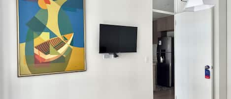 A modern hotel room with a large abstract painting, a flat-screen TV, a refrigerator, and a bed.