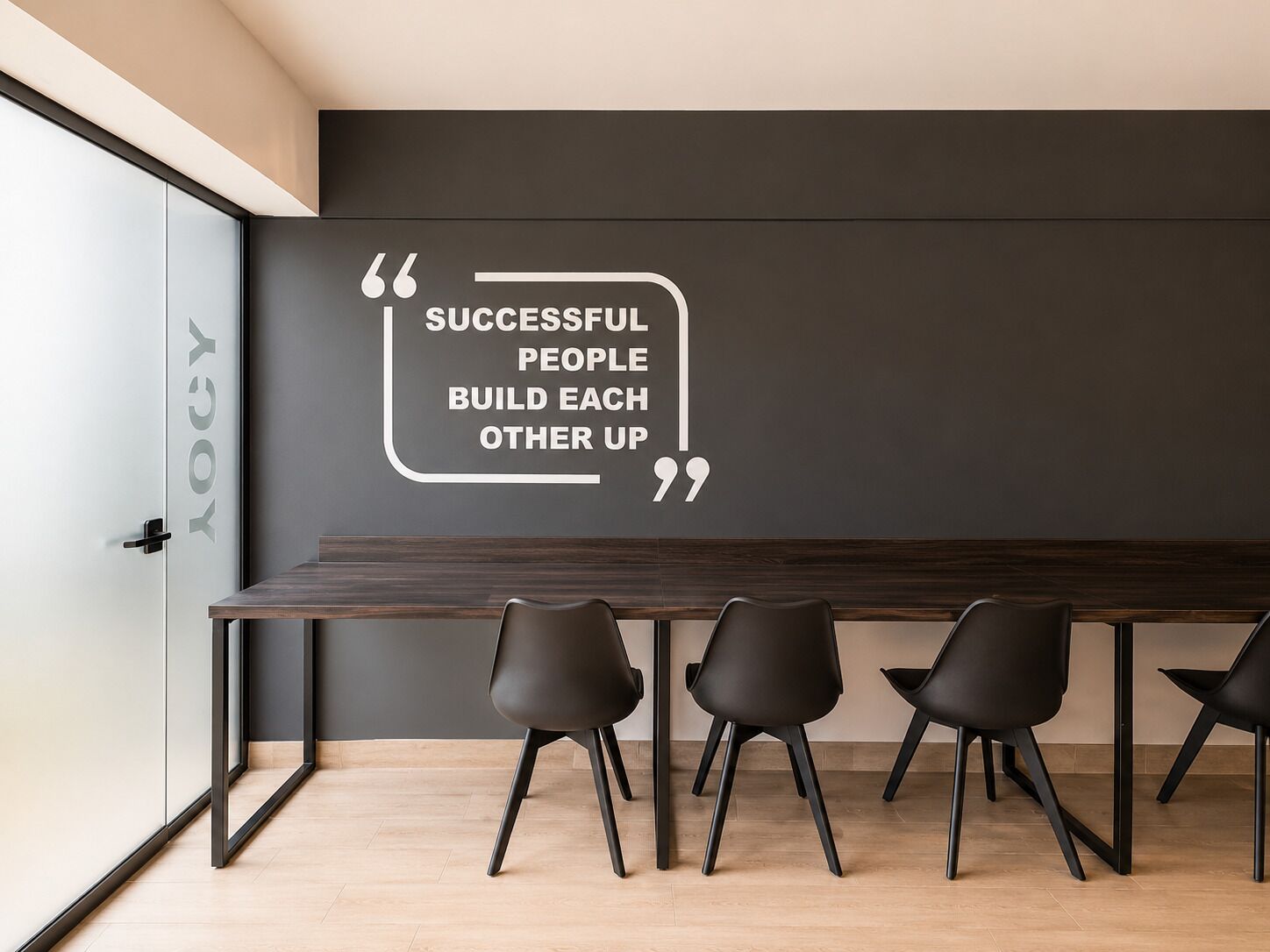 Une salle de réunion moderne avec un mur foncé, une citation et quatre chaises noires.