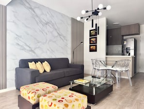 A modern living room with a marble wall, a gray sofa, clear glass coffee table, and ottomans with a fruit pattern. - Cozy Apartment in Jesús María (Jesús María)