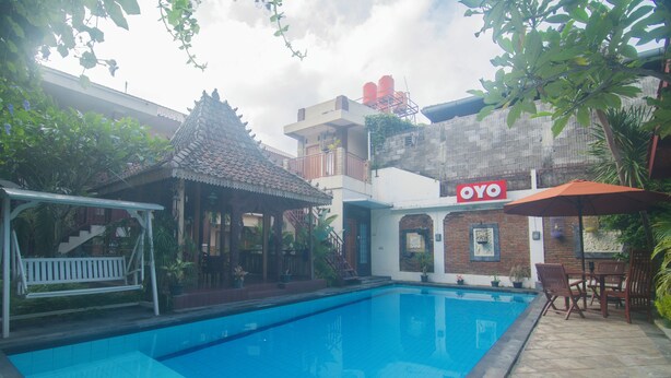 En swimmingpool med ett kaklat poolområde, en överbyggd sittplats och en byggnad med en skylt som visar texten ”OYO”.
