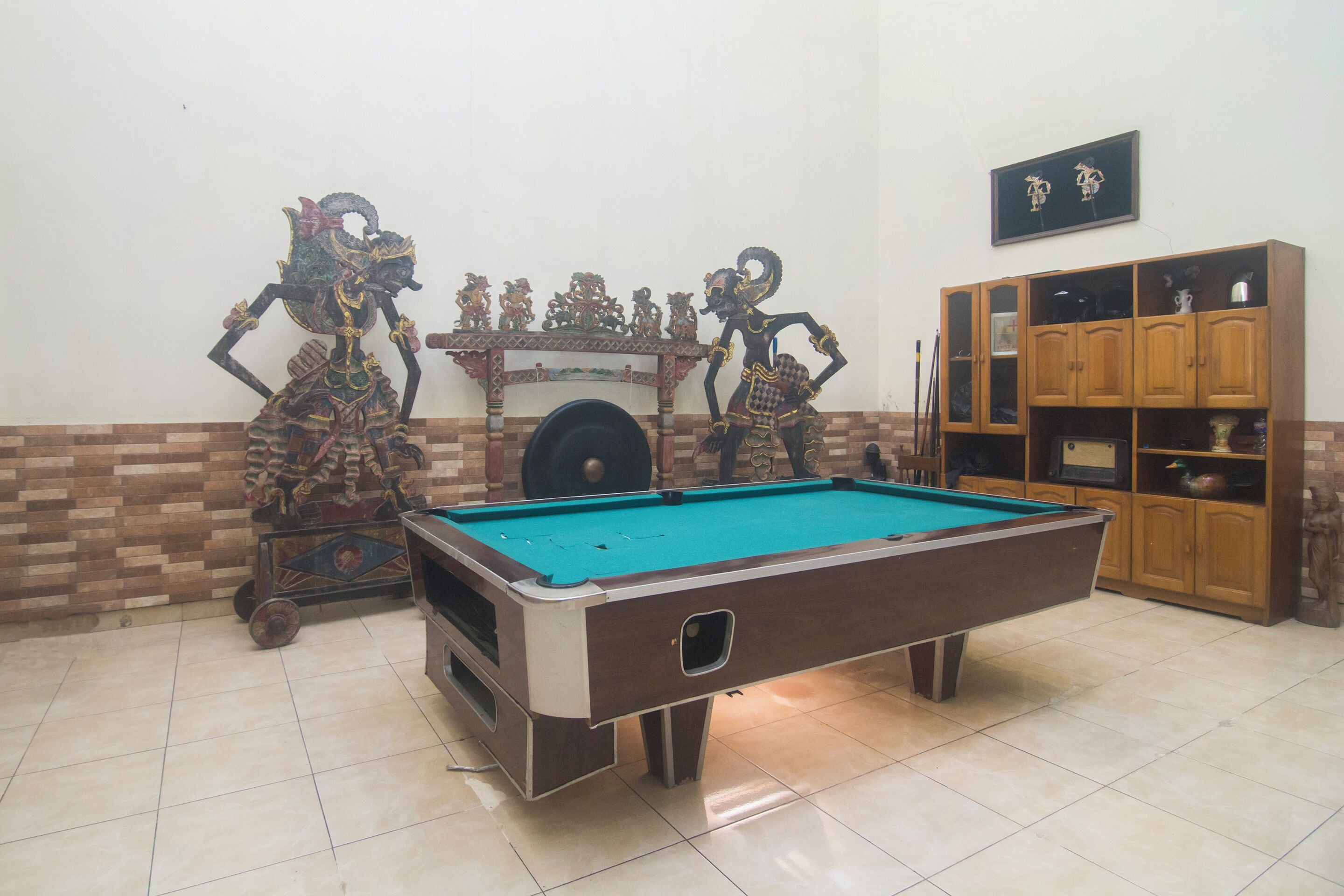 Una mesa de billar con un fondo decorativo, un aparador de madera con puertas de vidrio y un suelo de baldosas.