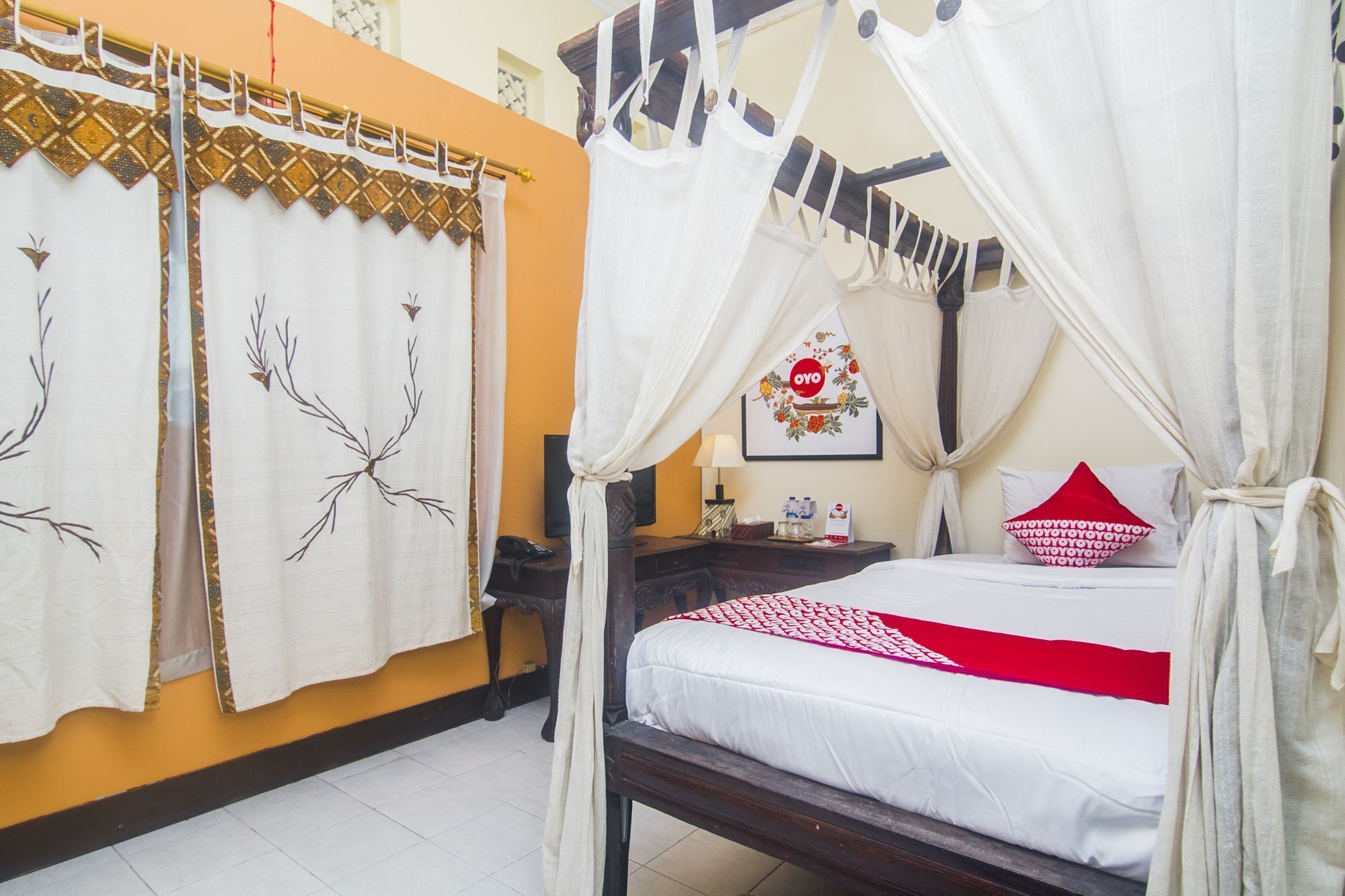 A room with a bed under a canopy, a nightstand with a lamp, and a wall with a framed picture.