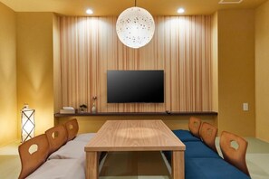A room with a flat-screen TV mounted on a wooden wall, a wooden table, and two sofas with cut-out backrests.