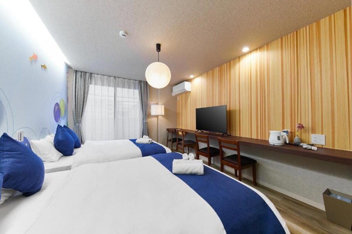 A hotel room with two beds, a desk with a television, and a wall-mounted air conditioner.