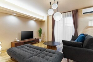 A modern living room with a flat-screen TV, a sofa, a round coffee table, and a potted plant.