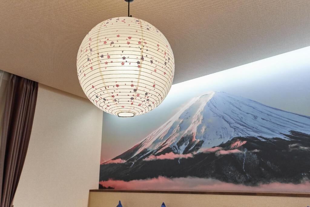 A room with a large wall mural of a mountain, a hanging spherical light fixture, and a partial view of a bed.