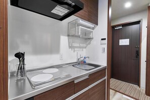 A modern kitchen with a stainless steel countertop, a built-in oven, and a microwave. There is a sink with a faucet and a utensil holder. The kitchen has wooden cabinets and a dark wooden door in the background.