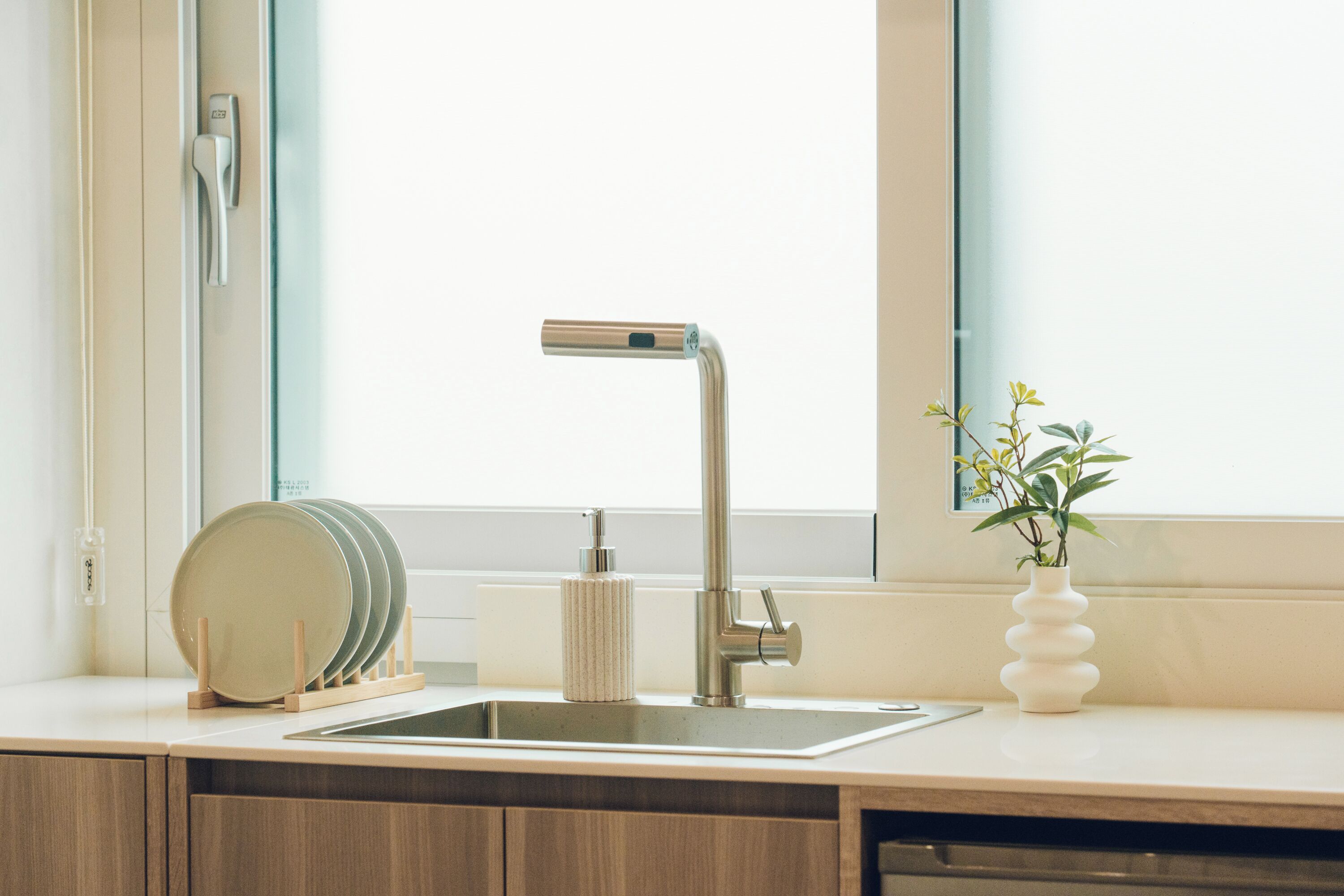 Una cocina moderna con un lavamanos de acero inoxidable, un armario de madera y una planta en el alféizar.