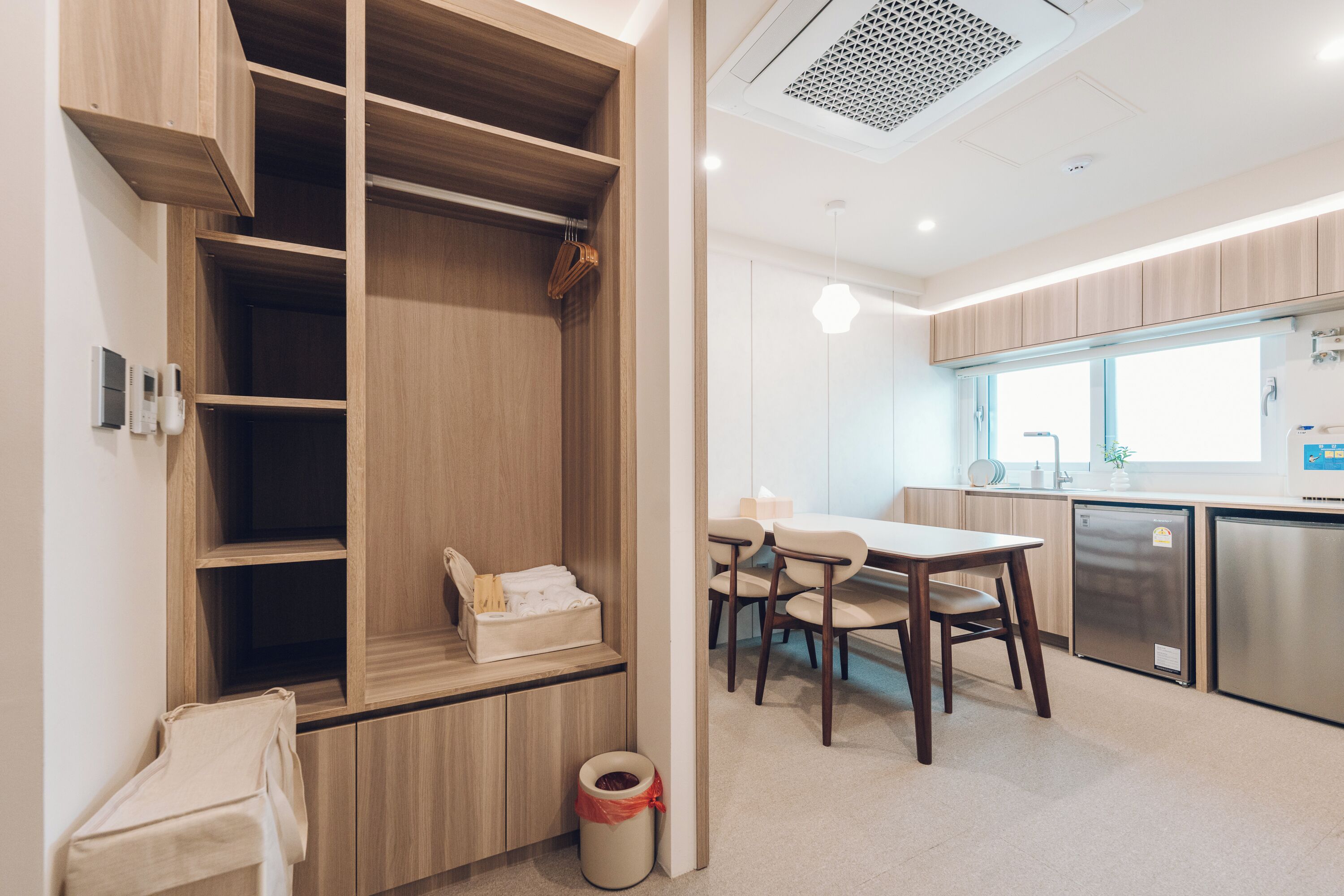 A modern kitchen with built-in appliances, a dining area with a table and chairs, and a wooden storage unit with shelves.