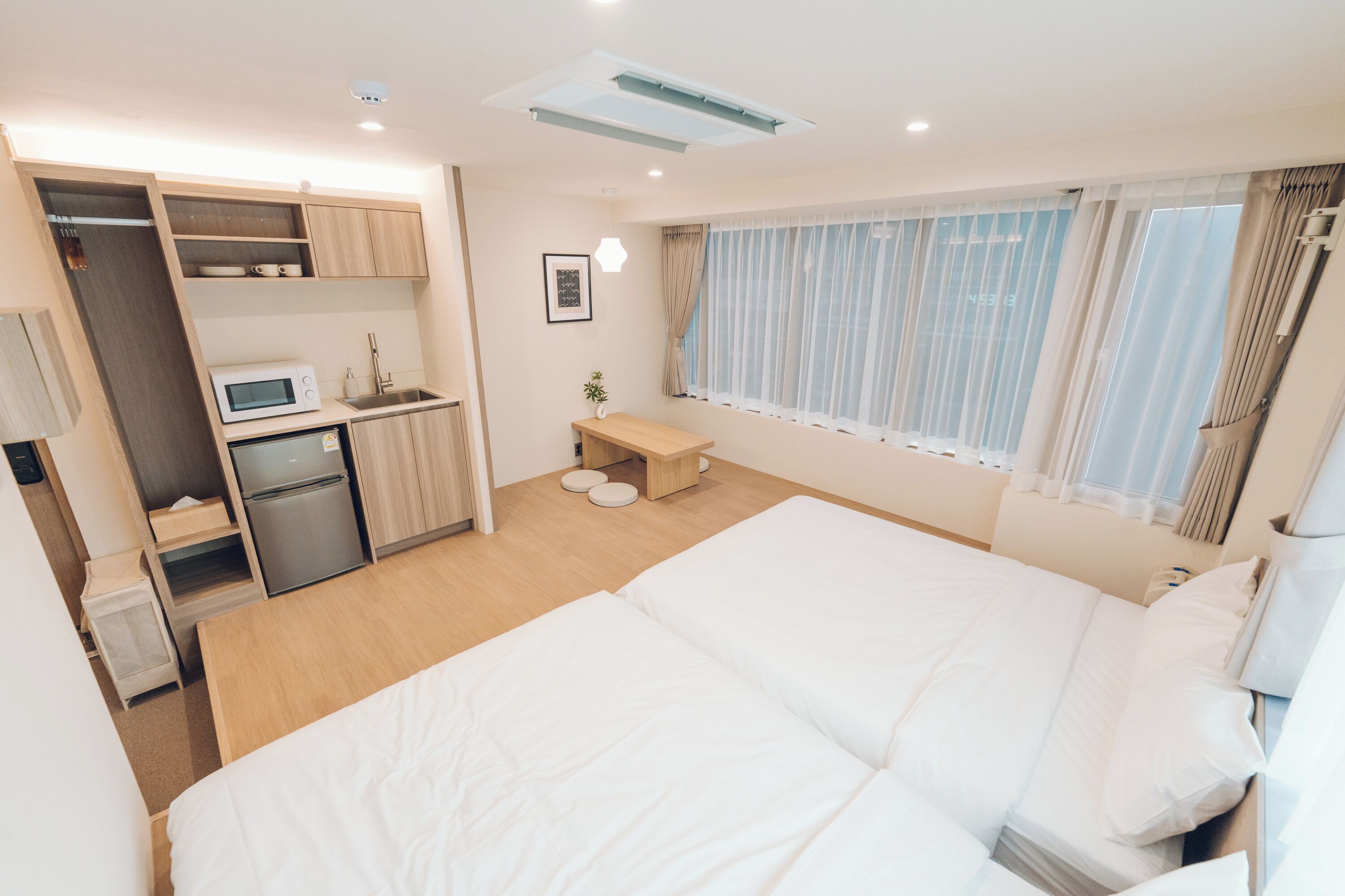 Habitación de hotel compacta con cama, kitchenette, una pequeña zona de estar y ventana con cortinas.