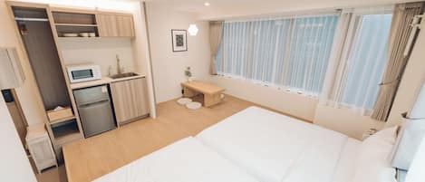 Habitación de hotel compacta con cama, kitchenette, una pequeña zona de estar y ventana con cortinas.
