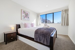 A bedroom with a bed, a nightstand, a lamp, a window with curtains, and a painting on the wall. - Entire home in Christchurch, New Zealand (Christchurch)