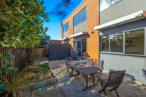 A modern building with a patio area featuring a table and chairs, a wooden fence, and a garden with plants. - Entire home in Christchurch, New Zealand (Christchurch)