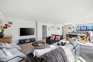 A modern living room with a flat-screen TV, a sofa, a coffee table, and a dining area with a kitchen in the background. - Entire home in Christchurch, New Zealand (Christchurch)