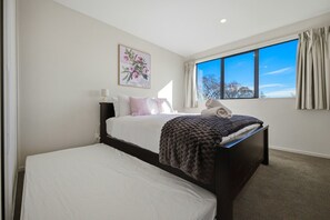 A hotel room with a bed, a bedside table, a lamp, a window with curtains, and a painting on the wall. - Entire home in Christchurch, New Zealand (Christchurch)