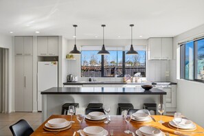 A modern kitchen with a central island, pendant lighting, and a dining area set for six. - Entire home in Christchurch, New Zealand (Christchurch)