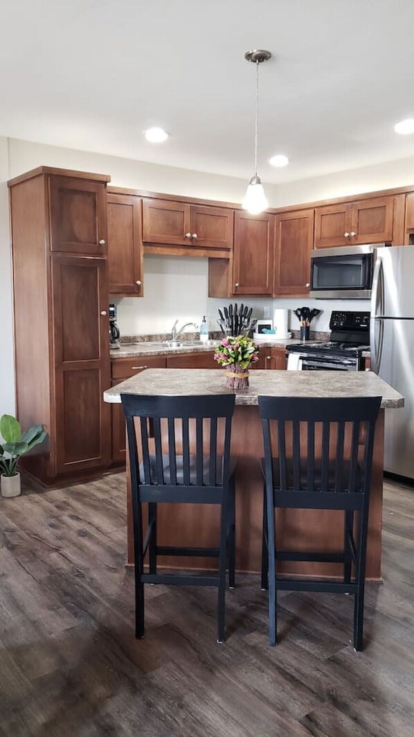 A modern kitchen with wooden cabinets, a stainless steel refrigerator, a microwave, and a central island with two chairs.