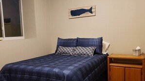 A bedroom with a bed, a nightstand, a wooden headboard, and a wall-mounted fish decoration.