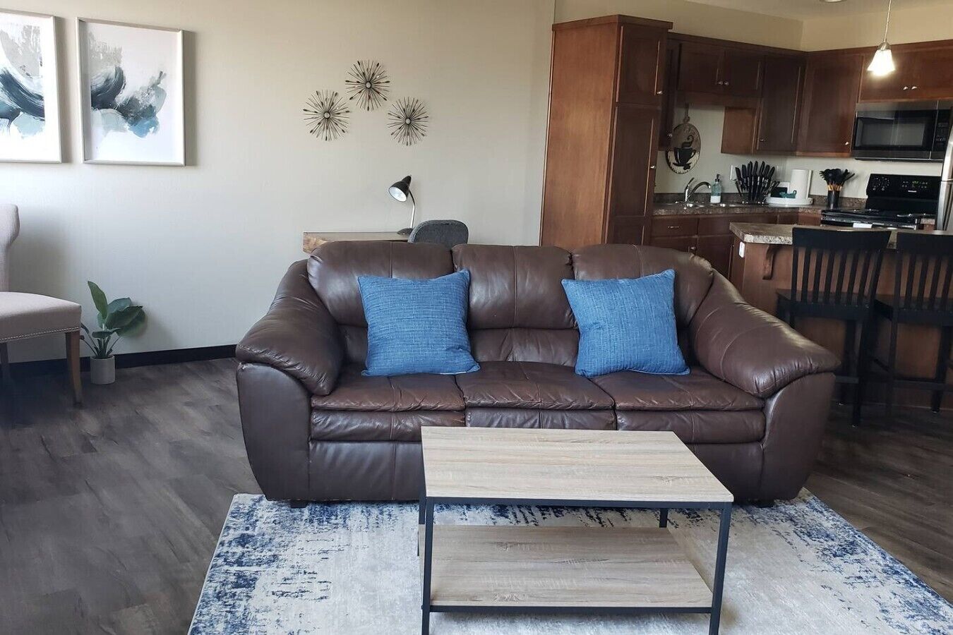 A living room with a brown leather sofa, two blue cushions, a small wooden coffee table, and a patterned rug.