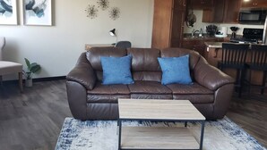 A living room with a brown leather sofa, two blue cushions, a small wooden coffee table, and a patterned rug.