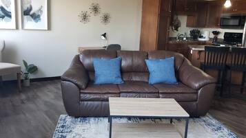 A living room with a brown leather sofa, two blue cushions, a small wooden coffee table, and a patterned rug.
