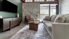 A living room with a sofa, a coffee table, a TV, a chair, and a patterned wall. - Landing | Spectacular 1BD, Rooftop Lounge, Gym (Jacksonville)