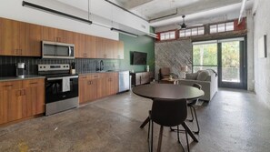 A modern kitchen with wooden cabinets, a built-in microwave, and a dining area with a round table and chairs. - Landing | Spectacular 1BD, Rooftop Lounge, Gym (Jacksonville)