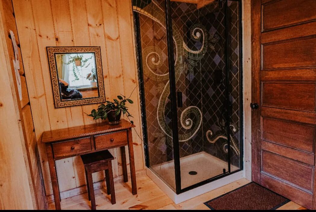 Un intérieur en bois avec un bureau en bois, un tableau encadré et une cabine de douche en verre ornée de motifs décoratifs.