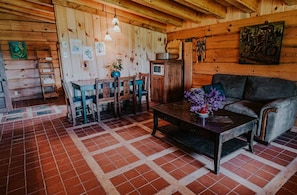 A rustic wooden interior with a dining area, a sofa, and a tiled floor.