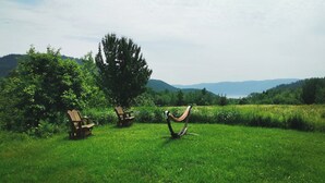 A grassy field with two wooden chairs and a hammock.